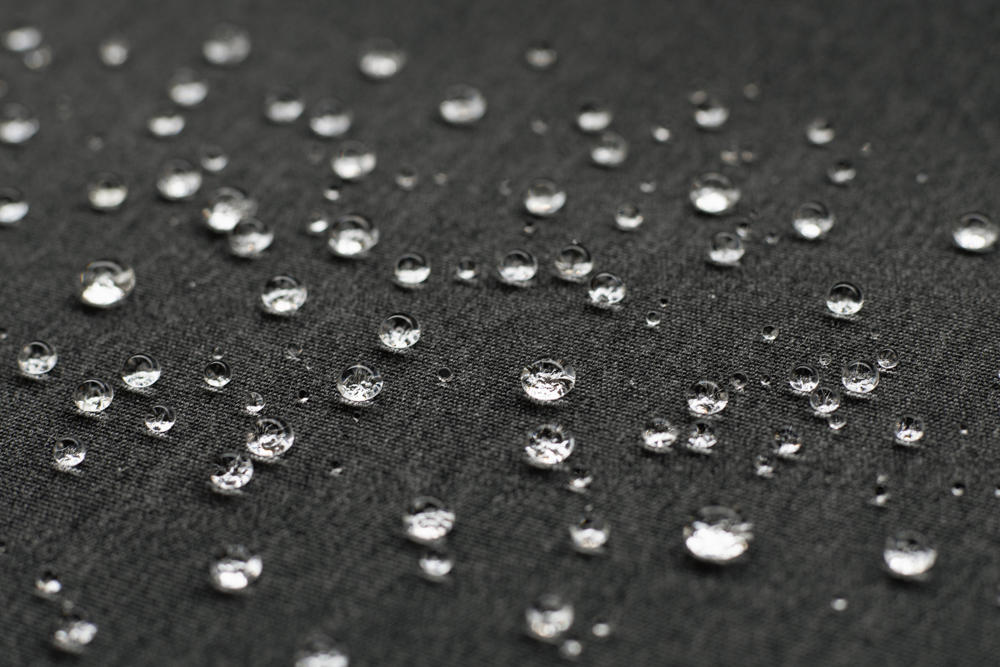 Kapljice vode na vodoodbojni črni tkanini, ki prikazujejo zaščitne lastnosti materiala za zunanje tende.