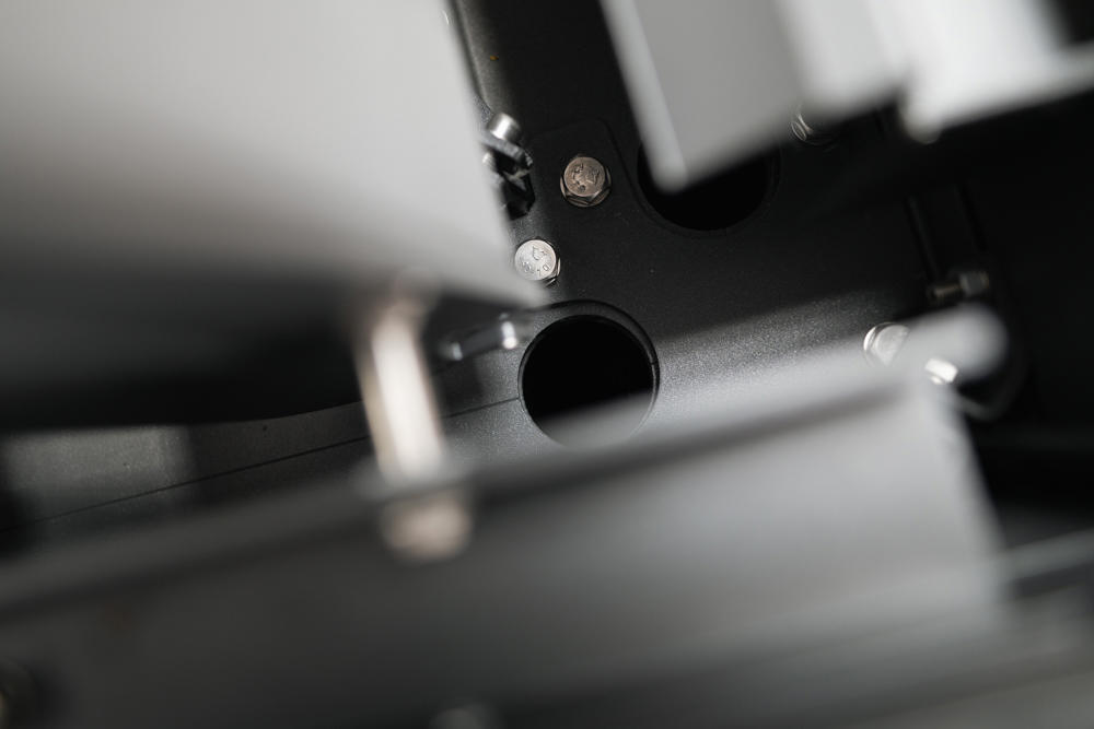 Makro posnetek notranjega mehanskega dela pergole z vidnimi vijaki, kovinskimi spoji in odprtino za sestavne elemente.