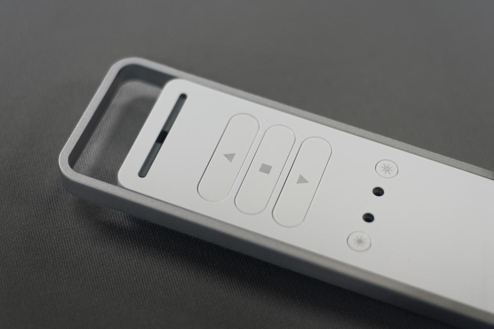 Daljinski upravljalnik za nadzor senčil in osvetlitve, s sodobnim minimalističnim dizajnom v sivi barvi.