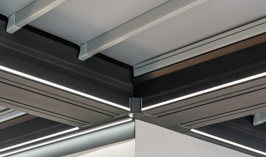 Detajl stropa moderne pergole z integrirano LED osvetlitvijo in aluminijasto konstrukcijo v temni barvi.
