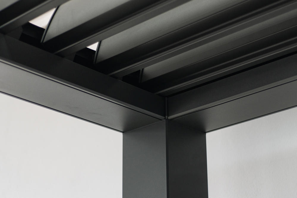 Bližnji posnetek notranjega vogala aluminijaste konstrukcije bioklimatske pergole v črni barvi.